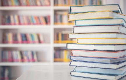 Stapel Bücher auf einem Tisch vor einem Bibliotheksregal
