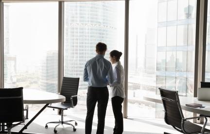 Zwei Personen stehen an einer Fensterfront im Büro und sprechen miteinander